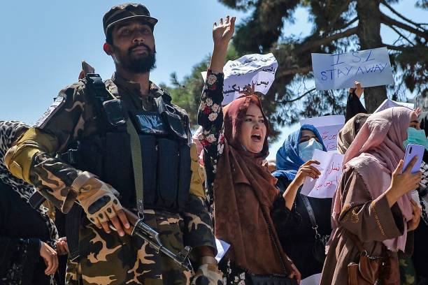 Afghan women shout slogans next to a Taliban fighter during an anti-Pakistan demonstration near the Pakistan embassy in Kabul on September 7, 2021. - The Taliban on September 7, 2021 fired shots into the air to disperse crowds who had gathered for an anti-Pakistan rally in the capital, the latest protest since the hardline Islamist movement swept to power last month. (Photo by Hoshang Hashimi / AFP) (Photo by HOSHANG HASHIMI/AFP via Getty Images)